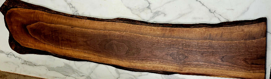 A long attractive live edge black Walnut grazing board with interesting wood patterns and a slight bend in the board