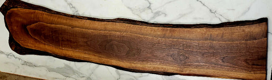 A long attractive live edge black Walnut grazing board with interesting wood patterns and a slight bend in the board