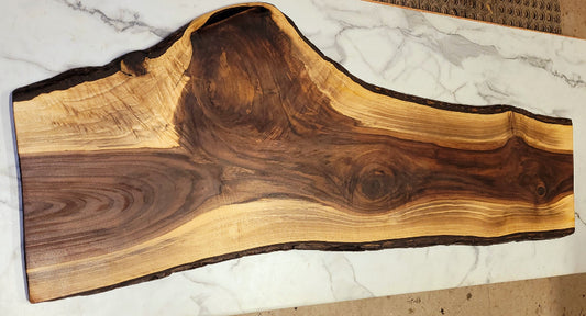 A large black walnut live edge grazing board with exciting patterns in its dark interior, surrounded by light colouring wood and black bark.