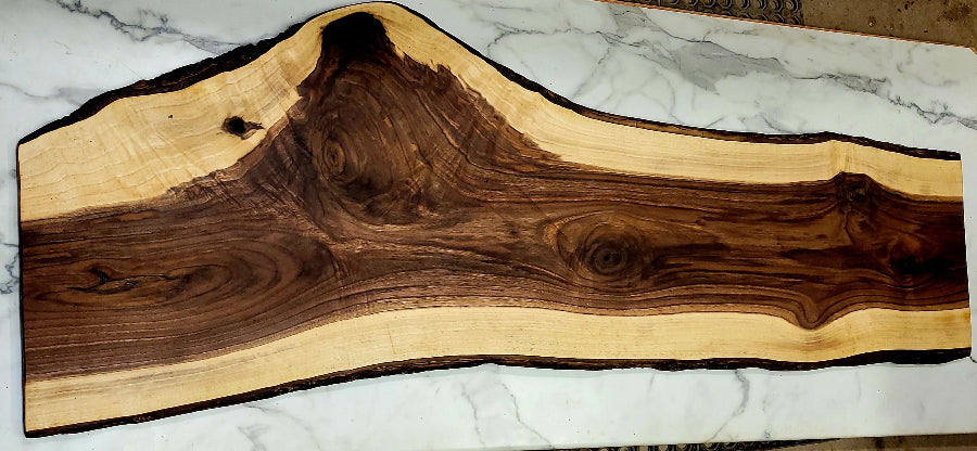 A beautiful live edge black Walnut grazing board with an irregular shape, a dark interior, light around the edges, with black bark